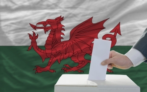 man putting ballot in a box during elections in wales in front of flag