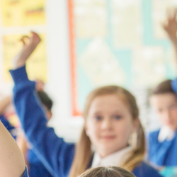 Image of school children with their hands up.