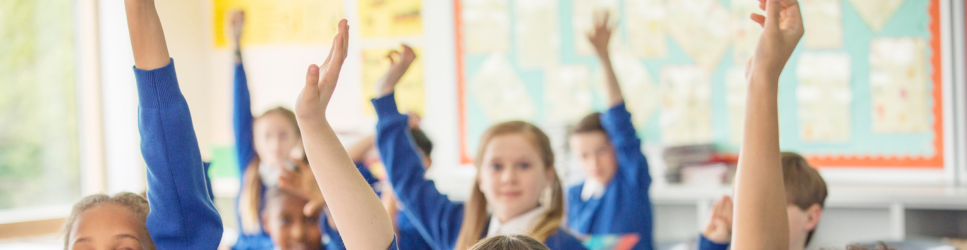 Image of school children with their hands up.