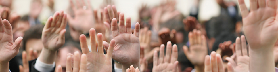 Image of a room full of employees holding their hands up to vote.